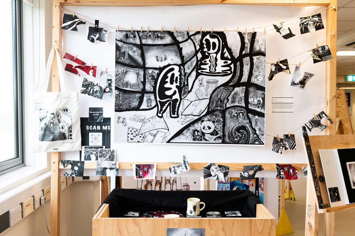 A display of different printmaking and illustration items; tote bags, postcards, and a large illustration in the middle.